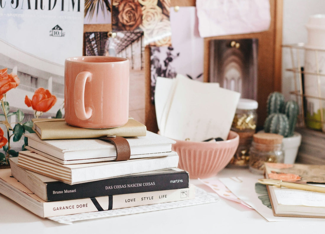A pink mug on a stack of books on a desk with stationery
