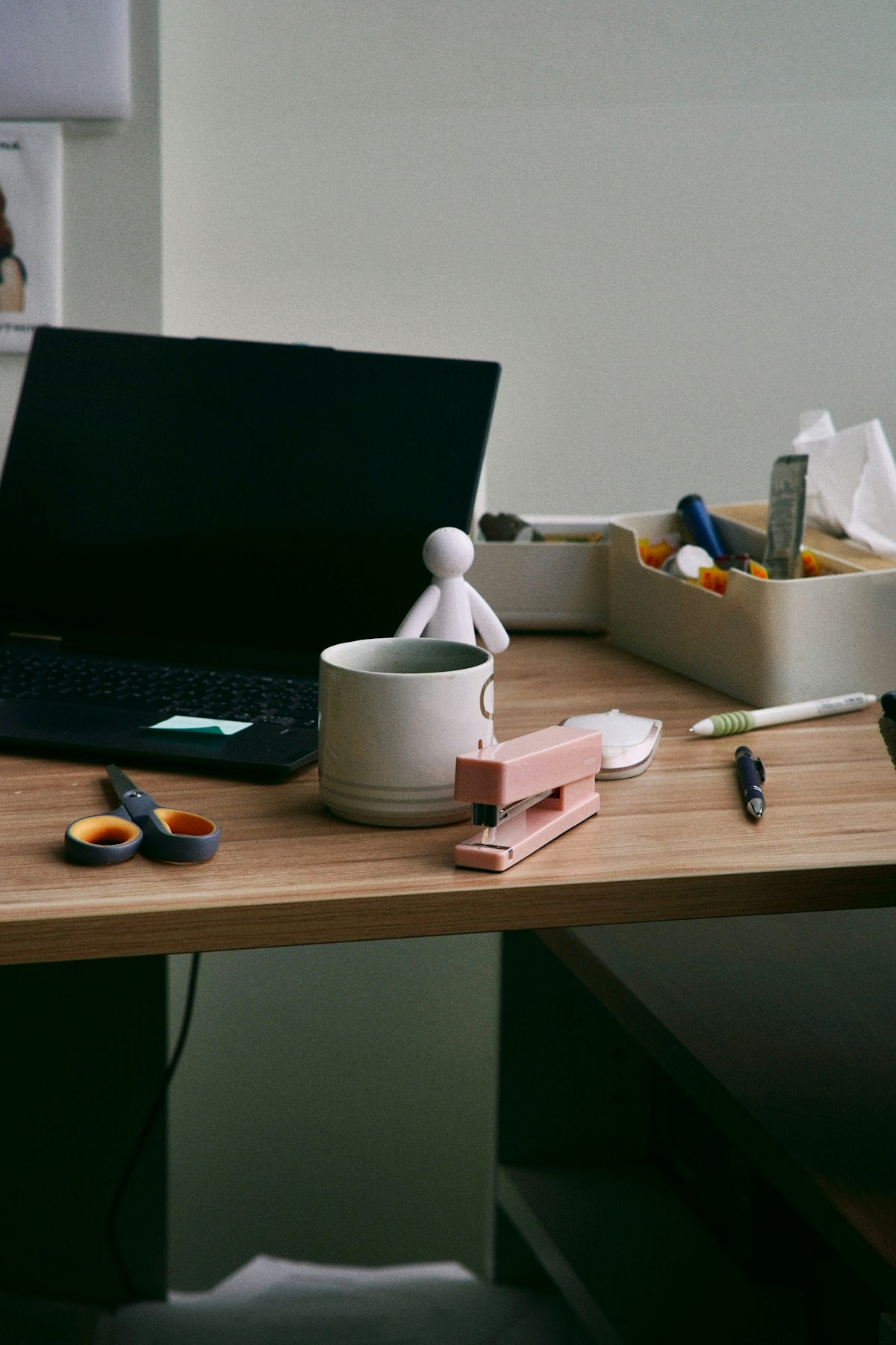 Wooden desk with laptop, stapler, mug, and office supplies.